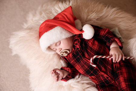 Cute baby in Santa hat with candy cane sleeping on soft faux fur, top view. Christmas seasonの写真素材