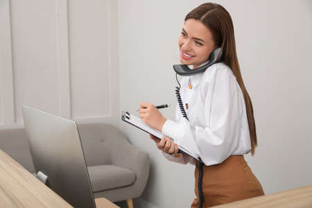 Female receptionist with clipboard talking on phone at workplaceの写真素材