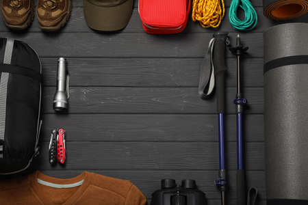 Frame made with trekking poles and other hiking equipment on dark gray wooden background, flat lay....