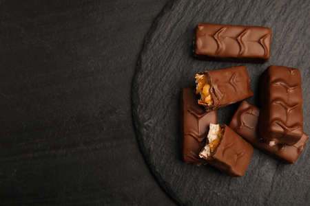 Slate plate of chocolate bars with caramel, nuts and nougat on black table, top view. Space for textの写真素材