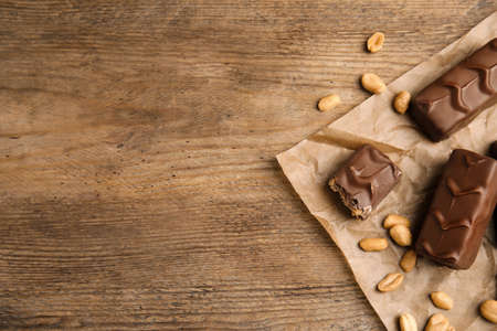 Chocolate bars with nuts and parchment on wooden table, flat lay. Space for textの写真素材