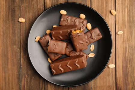 Plate of chocolate bars with caramel, nuts and nougat on wooden table, top viewの写真素材