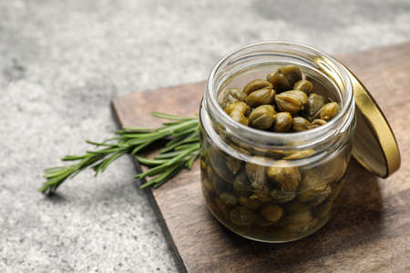 Tasty capers in glass jar and rosemary on gray table, space for textの写真素材