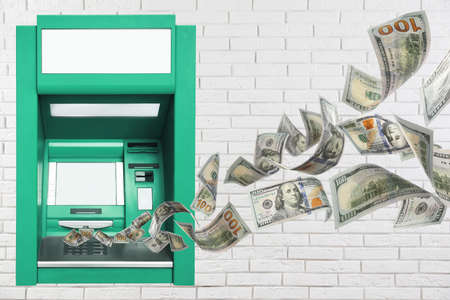 Modern automated cash machine on white brick wall and flying moneyの写真素材