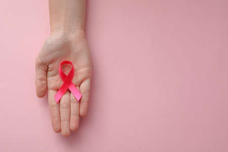 Woman holding pink ribbon on color background, top view with space for text. Breast cancer awareness...