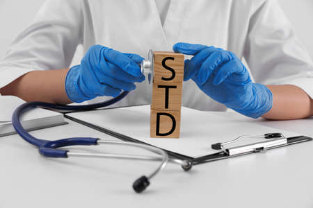 Doctor and wooden cubes with abbreviation STD at white table, closeupの写真素材