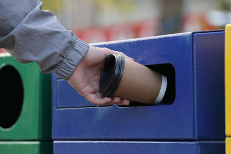 Man throwing paper coffee cup into garbage bin outdoors, closeup. Waste sortingの写真素材