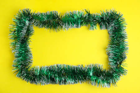 Frame of green tinsel on yellow background, top view. Space for textの写真素材