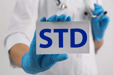 Doctor holding sheet of paper with abbreviation STD on white background, closeupの写真素材