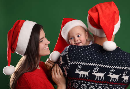 Happy couple with cute baby in Christmas outfits and Santa hats on green backgroundの写真素材