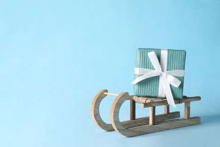 Wooden sleigh with Christmas gift box on light blue background, space for textの写真素材