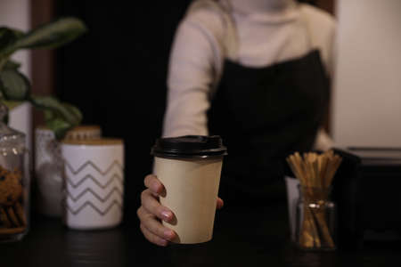 Barista putting takeaway coffee cup on table indoors, closeupの写真素材