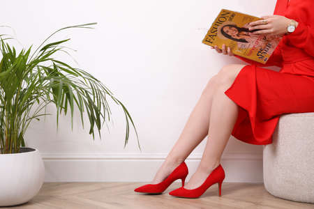 Woman reading fashion magazine near white wall indoors, closeupの写真素材