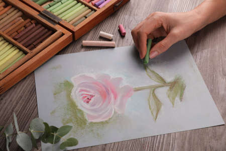 Woman drawing beautiful pink rose with soft pastel at wooden table, closeupの写真素材