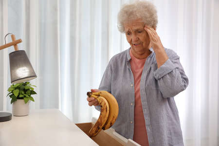 Senior woman finding bananas in chest of drawers at home. Age-related memory impairmentの写真素材