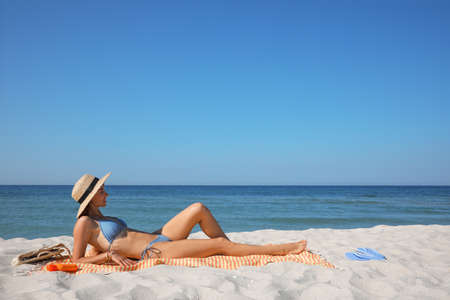 Woman with towel and other beach stuff on sand near sea