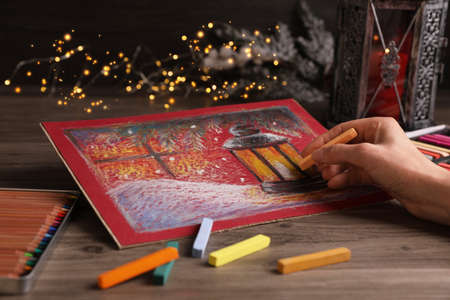 Woman drawing beautiful lantern with soft pastel at wooden table against blurred lights, closeupの写真素材