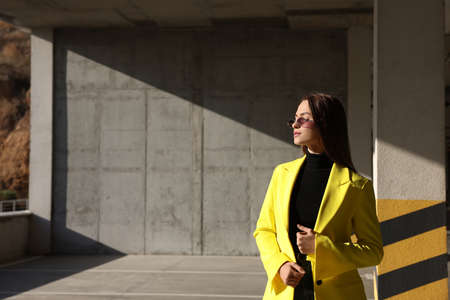 Fashionable young woman wearing stylish outfit with yellow jacket in open parking garage. Space for...