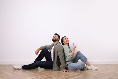 Young couple sitting on floor near white wall indoorsの写真素材