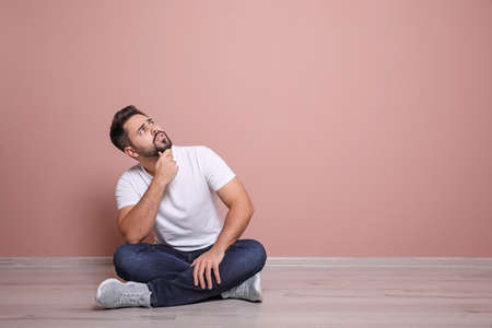 Young man sitting on floor near pink wall indoors. Space for textの写真素材