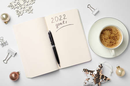 Inscription 2022 Goals written in planner, cup of coffee and Christmas decor on white background,...