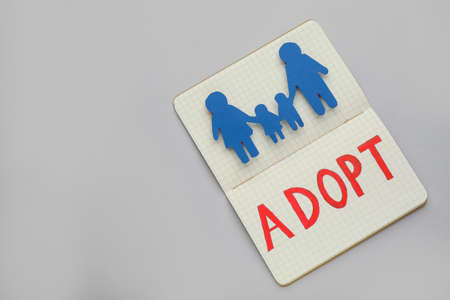 Notebook with family figure and word Adopt on gray background, top view. Space for textの写真素材
