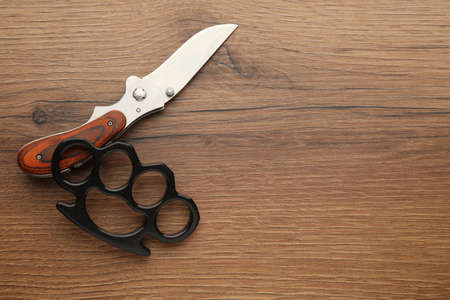Black brass knuckles and knife on wooden background, flat lay. Space for textの写真素材