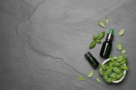 Bottles of essential basil oil and fresh leaves on dark gray table, flat lay. Space for textの写真素材