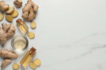 Glass bottles of essential oil and ginger root on white marble table, flat lay. Space for text