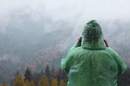 Woman in raincoat enjoying mountain landscape under rain, back viewの写真素材