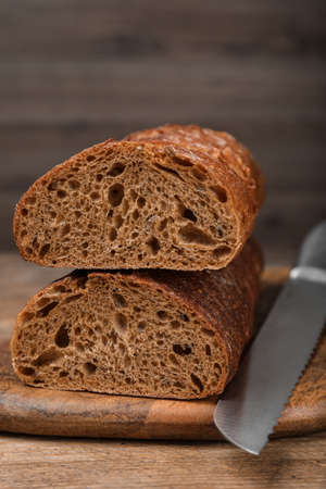 Cut rye baguette with knife on wooden table, closeup