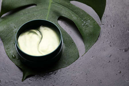 Package of under eye patches and tropical leaf on gray background. Cosmetic productの写真素材