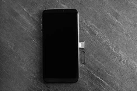 Mobile phone with Sim card in tray and ejector tool on gray table, flat lay