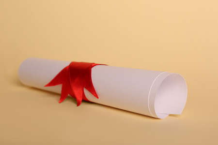 Rolled student's diploma with red ribbon on beige backgroundの写真素材