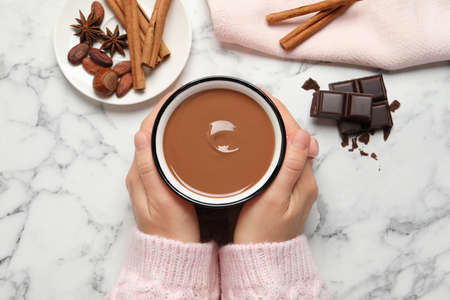 Woman with mug of yummy hot chocolate at white marble table, top view