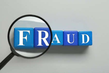 Wooden cubes with word Fraud and magnifying glass on light gray background, flat layの写真素材