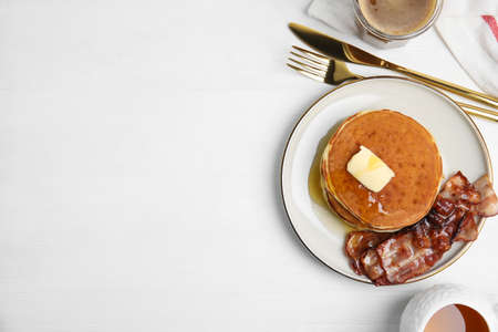 Delicious pancakes with maple syrup, butter and fried bacon on white wooden table, flat lay. Space for textの写真素材