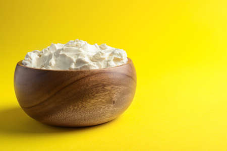 Bowl of tasty cream cheese on yellow background, space for textの写真素材