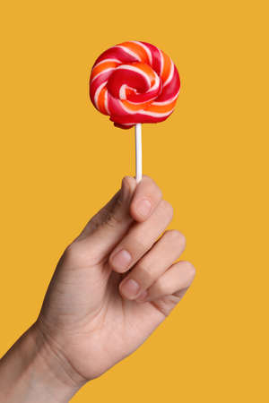 Woman holding bright tasty lollipop on orange background, closeupの写真素材