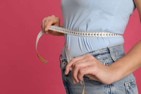 Woman measuring waist with tape on pink background, closeupの写真素材