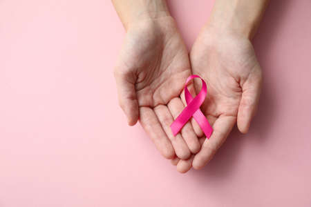 Woman holding pink ribbon on color background, top view with space for text. Breast cancer awareness...