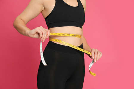 Woman measuring waist with tape on pink background, closeupの写真素材