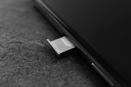 Mobile phone with Sim card in tray on gray table, closeup