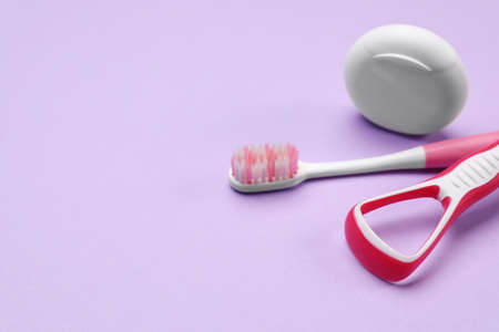 Red tongue cleaner, toothbrush and dental floss on violet background, closeup. Space for text