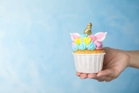 Woman holding cute sweet unicorn cupcake on light blue background, closeup. Space for textの写真素材