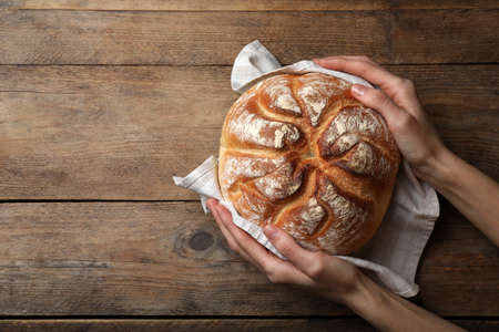 Woman holding loaf of tasty wheat sodawater bread at wooden table, top view. Space for textの写真素材