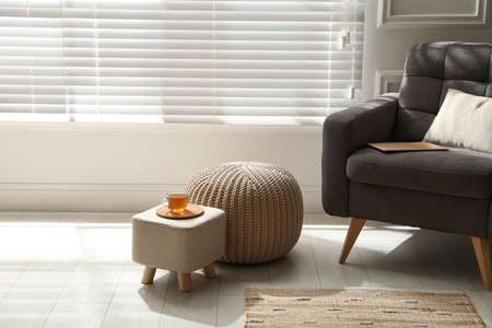 Tray with cup of tea on stylish ottoman and comfortable pouf in roomの写真素材