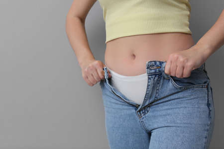Woman trying to put on tight jeans against light gray background, closeup. Space for textの写真素材
