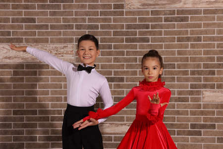 Beautifully dressed couple of kids dancing together near brick wall indoorsの写真素材