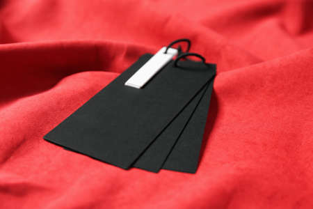 Blank black tags on red fabric, closeup. Space for textの写真素材